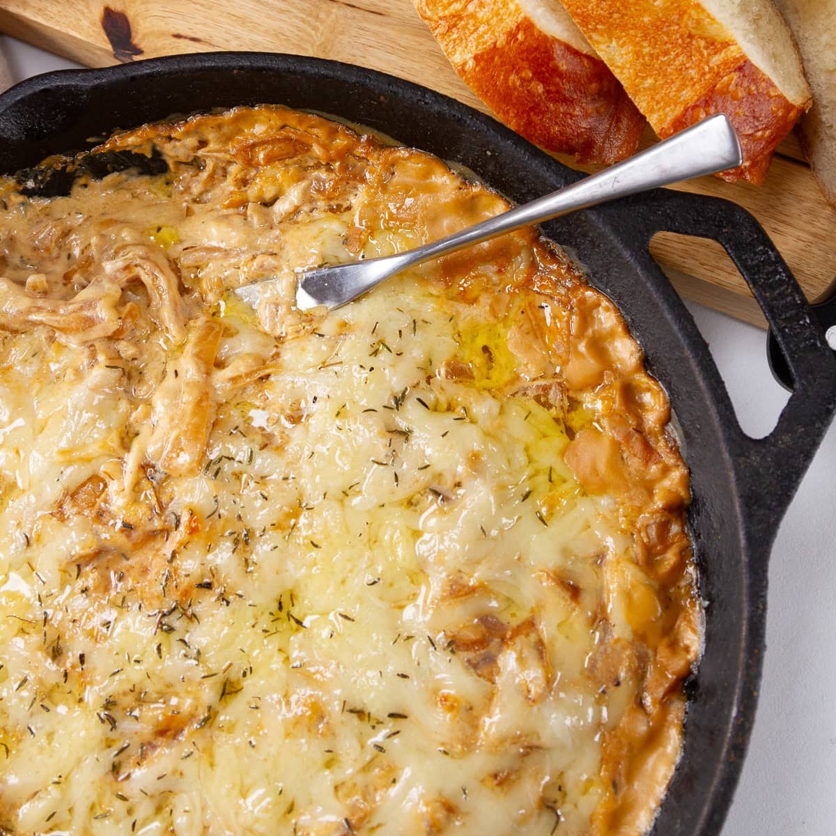 square crop of a cast iron skillet filled with creamy onion dip and a knife in the dip sliced bread next to the dip.