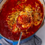 square crop looking down into a casserole dish with meatballs baked in marinara with cheese and a meatball being held up by a spoon.