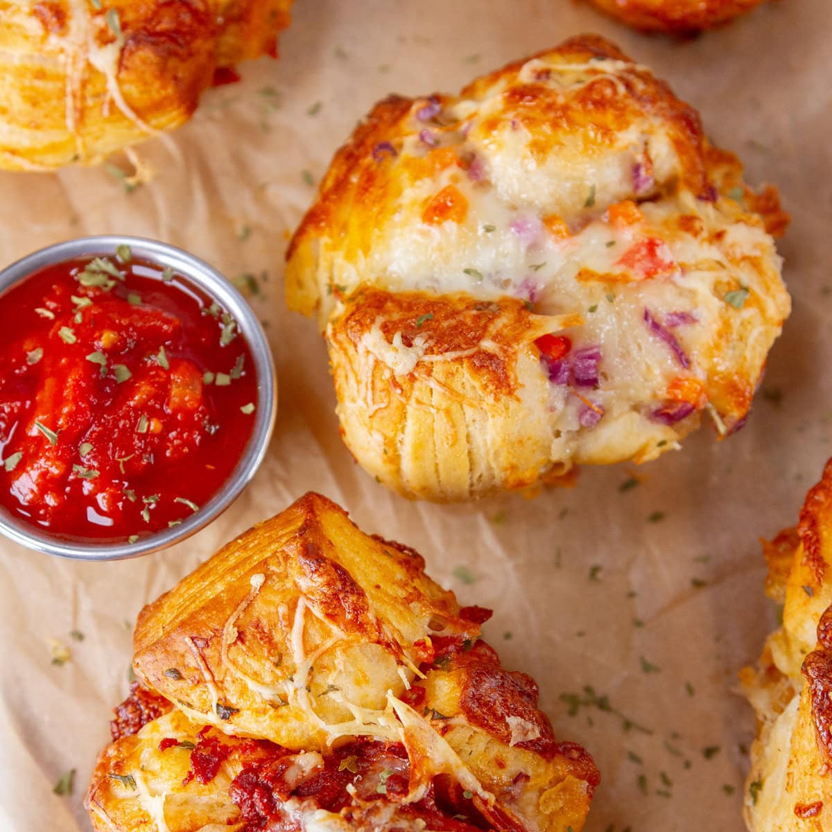 square crop of some pizza muffins on a piece of parchment paper with a small cup of marinara for dipping.