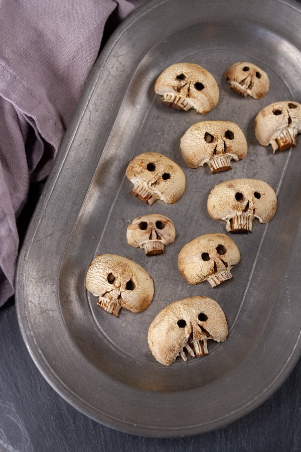 white mushrooms carved to look like skulls for Halloween on a pewter plate.