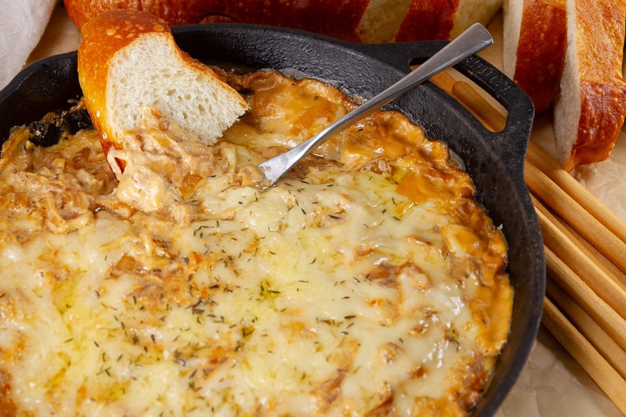 cheesy dip in a cast iron skillet with a knife and a piece of bread.