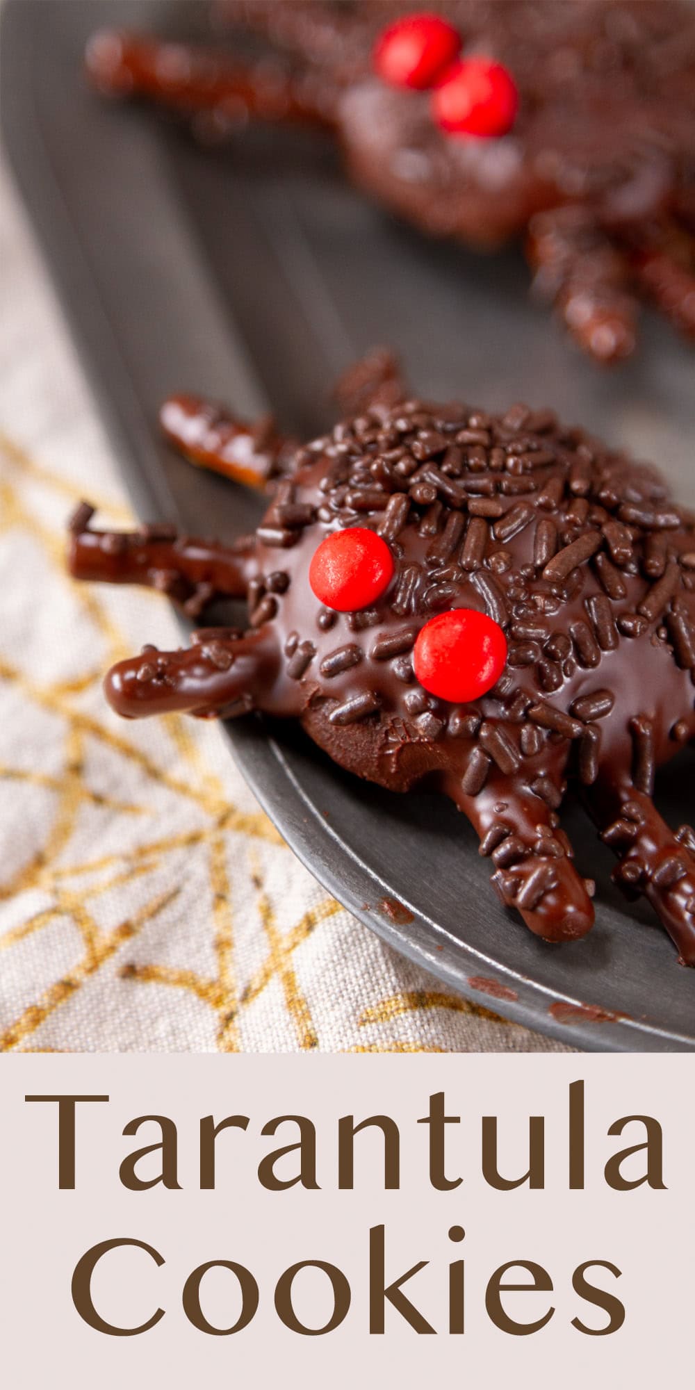 chocolate covered tarantula cookies on a pewter plate with a spider web towel underneath.