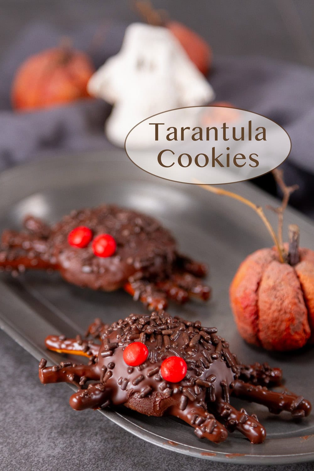 spider cookies covered in chocolate and sprinkles with Halloween decorations around.