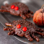 square crop of spider cookies on a pewter plate with a decorative pumpkin next to them.