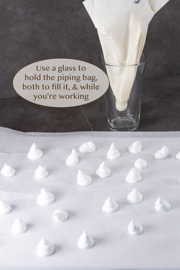 a glass holding a piping bag behind several meringues.