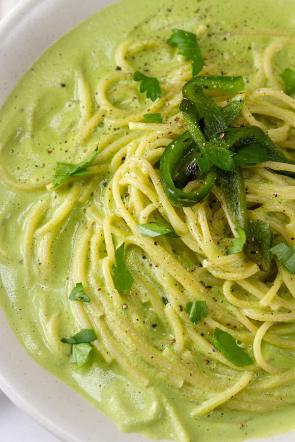 a bowl of pasta in poblano sauce with roasted poblano and parsley for garnish.