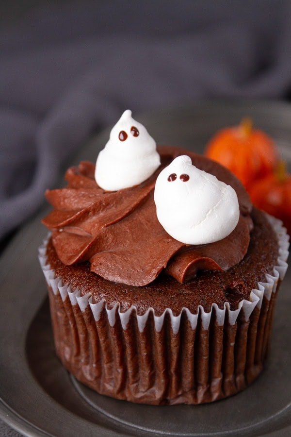 two meringue ghosts on a chocolate cupcake.