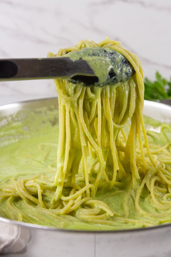 tongs serving up some noodles in creamy green sauce from a pan.