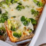 square crop of a piece of broccoli rice casserole being taken out of the casserole dish.