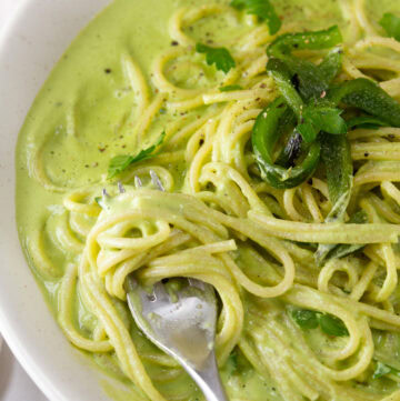 square crop of pasta in a green sauce with a fork twirling the pasta.