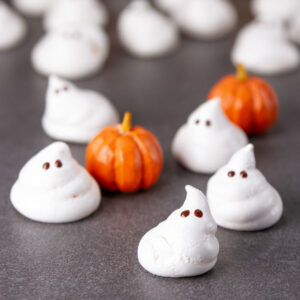 square crop of meringue ghosts on a gray background with small wooden pumpkins.