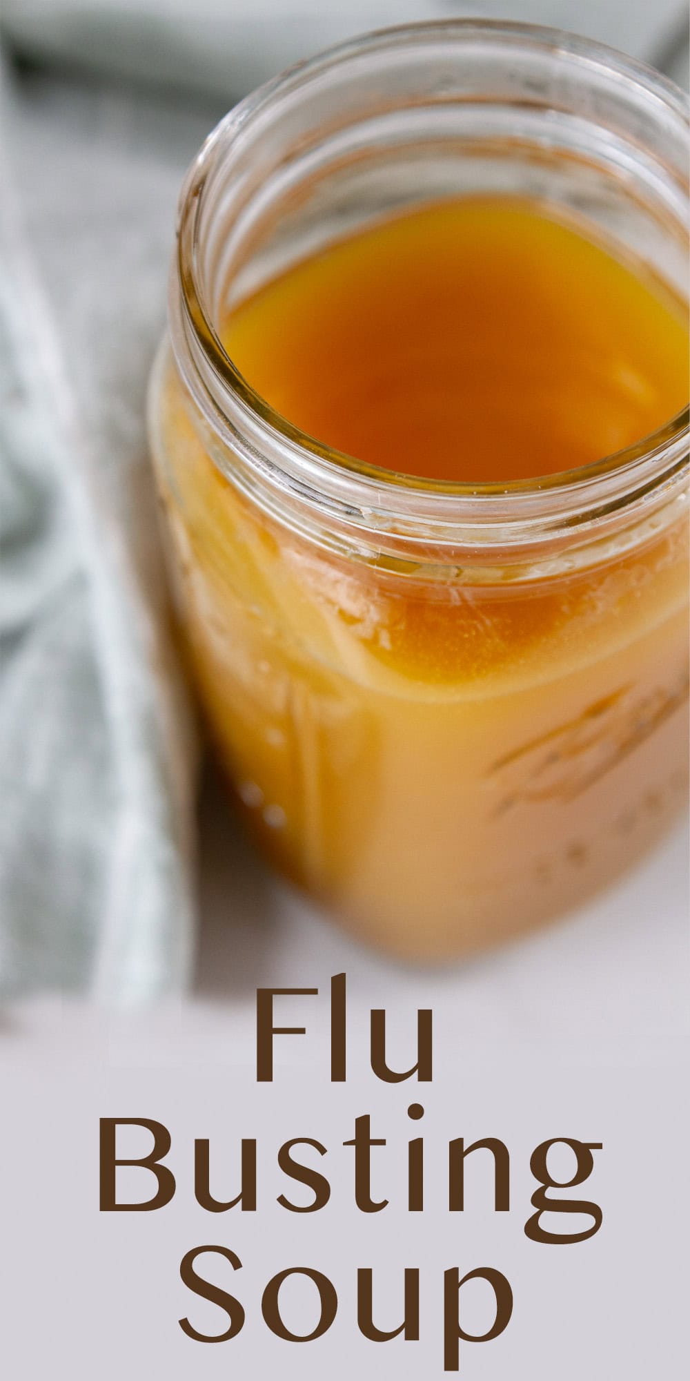 A mason jar filled with broth soup and a green cloth napkin behind it.