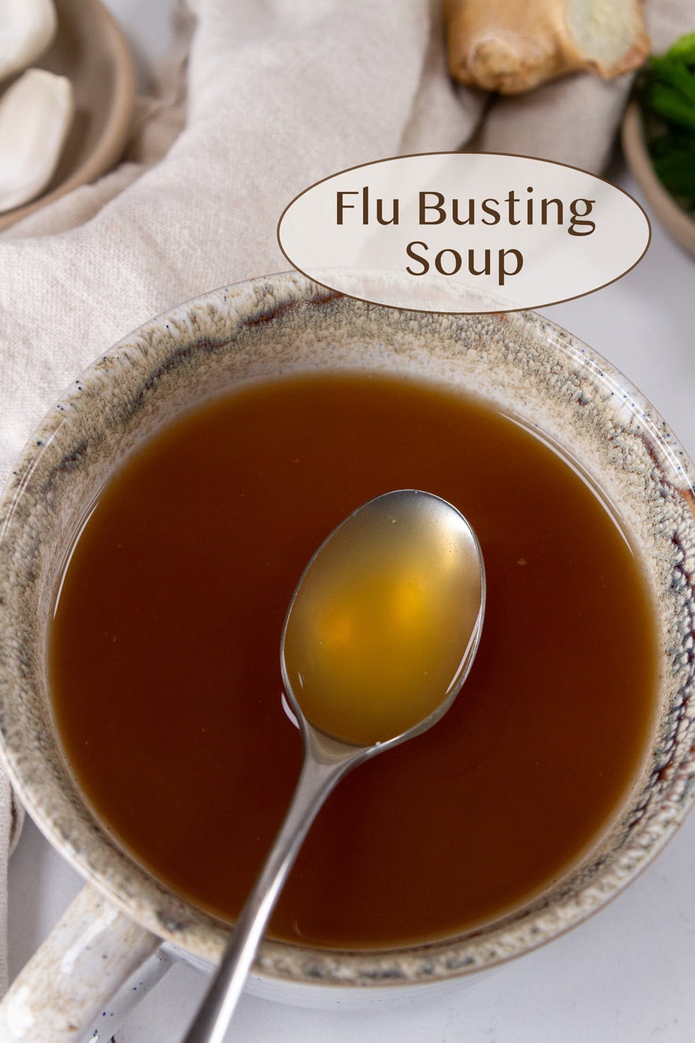 a mug filled with broth Flu Busting Soup and a spoon serving up a bite.