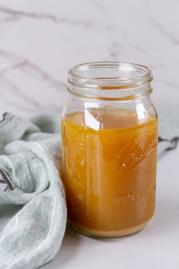 a mason jar filled with broth with a green cloth behind it.