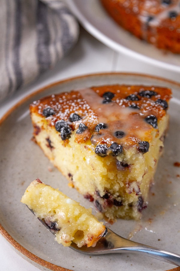 cake with lemon icing on a plate and a fork has taken a bite out of it.