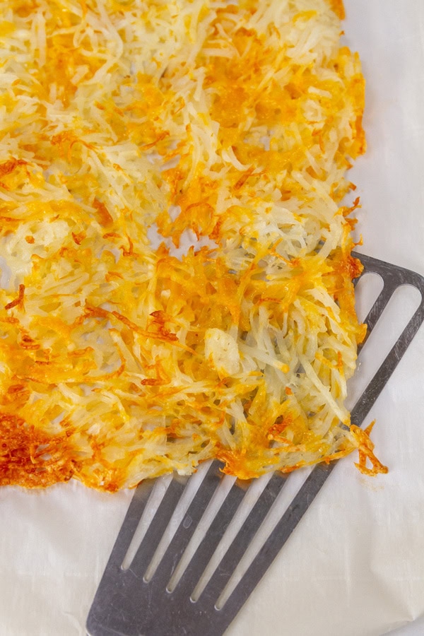 sheet pan hash browns on parchment paper with a metal spatula.