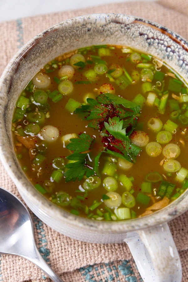 a mug of soup with lots of veggies added to it.