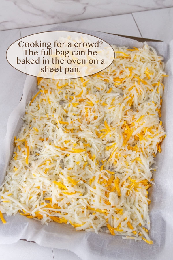 raw shredded potatoes on a baking tray with cheese ready to go in the oven.