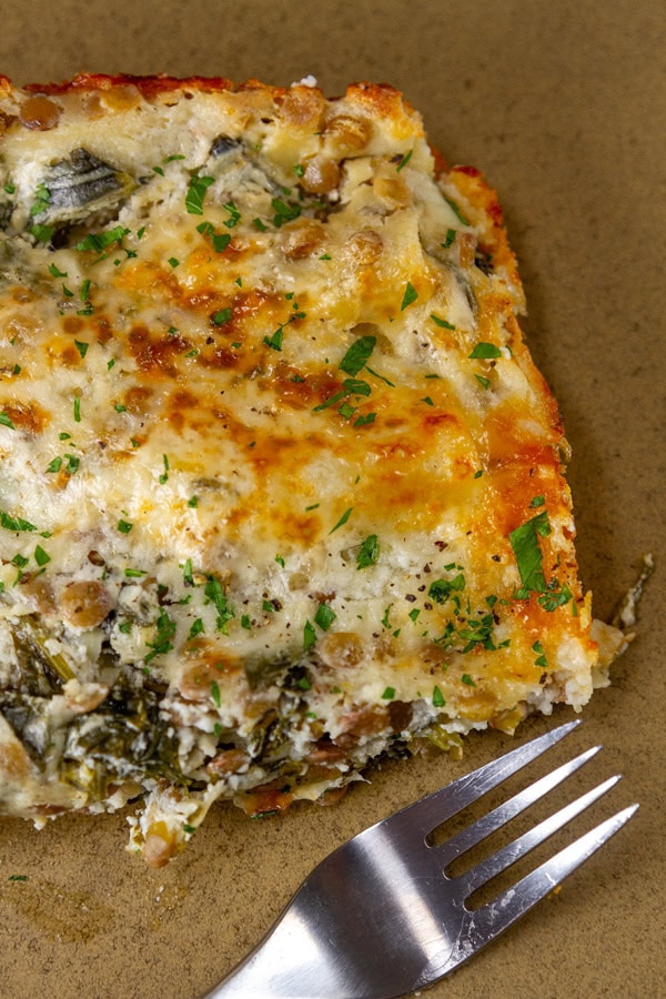 close up on a slice of white spinach lasagna with a fork next to it.