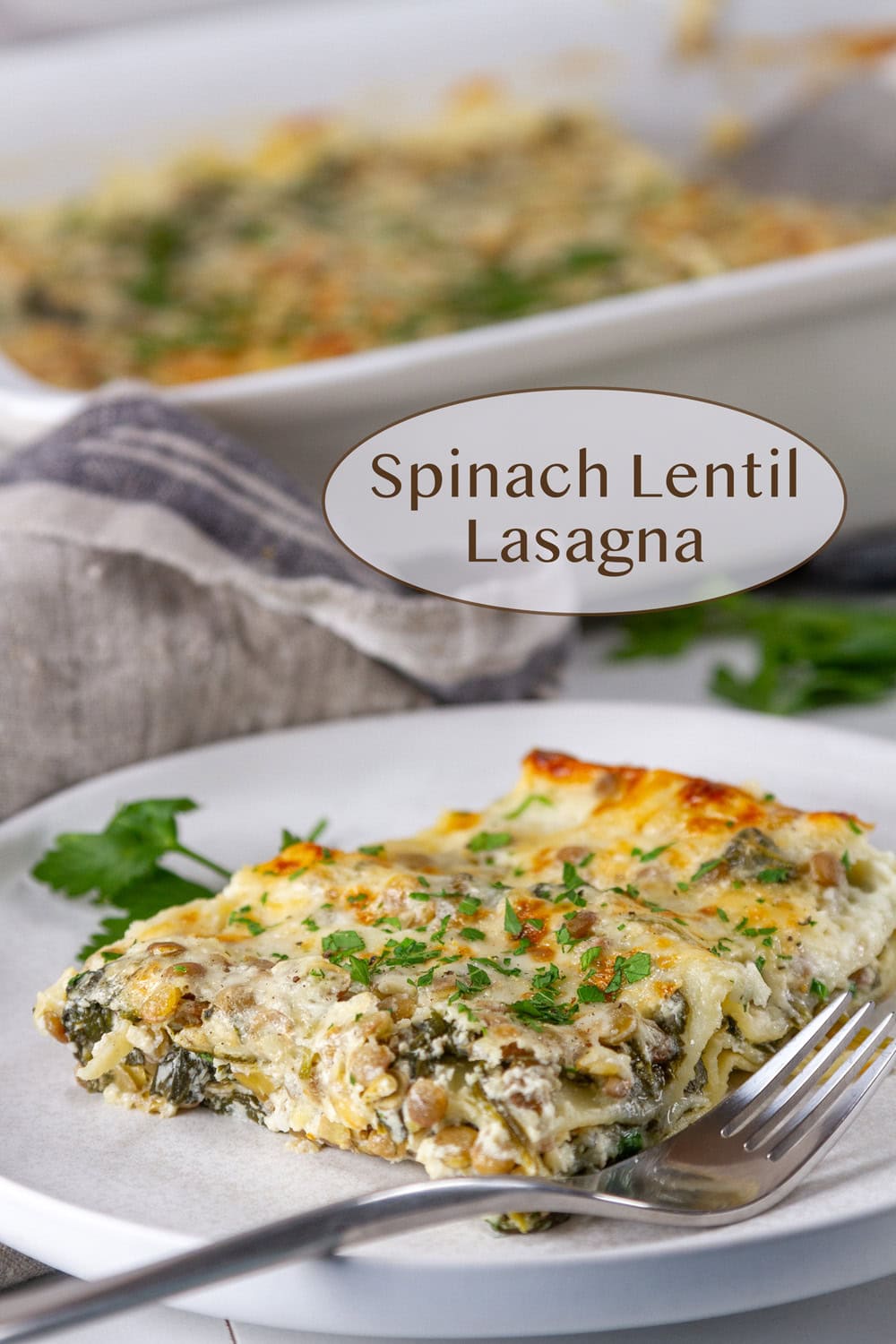 a slice of spinach lentil lasagna on a white plate in front of the casserole dish of lasagna. 