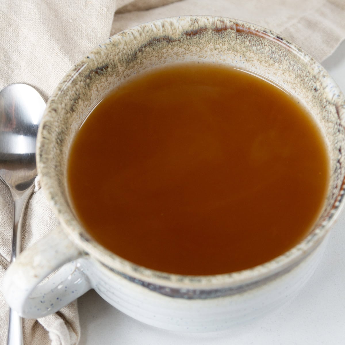 square crop of a mug of soup with a spoon to the left.