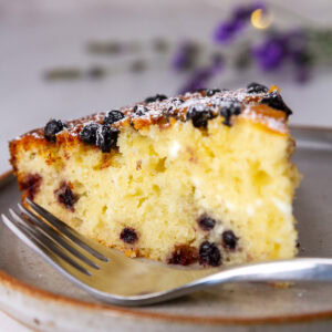 square crop of a slice of blueberry cake with a fork.