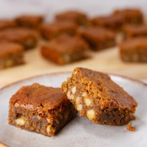 square crop of two cookie bars on a white plate in front of the rest of the batch of bars.