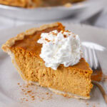 square crop of a slice of pumpkin pie on a plate with a fork.
