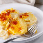 square crop of scalloped potatoes on a white plate.