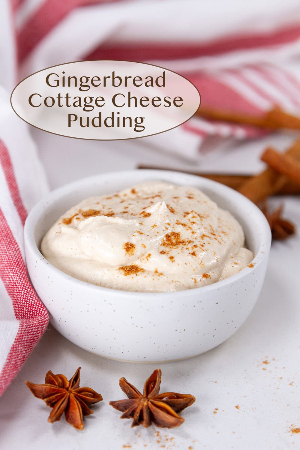 gingerbread pudding in a white cup with whole spices around it and a red towel.