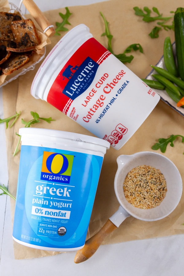 cottage cheese, Greek yogurt, and seasoning on parchment paper with veggies and crackers around.