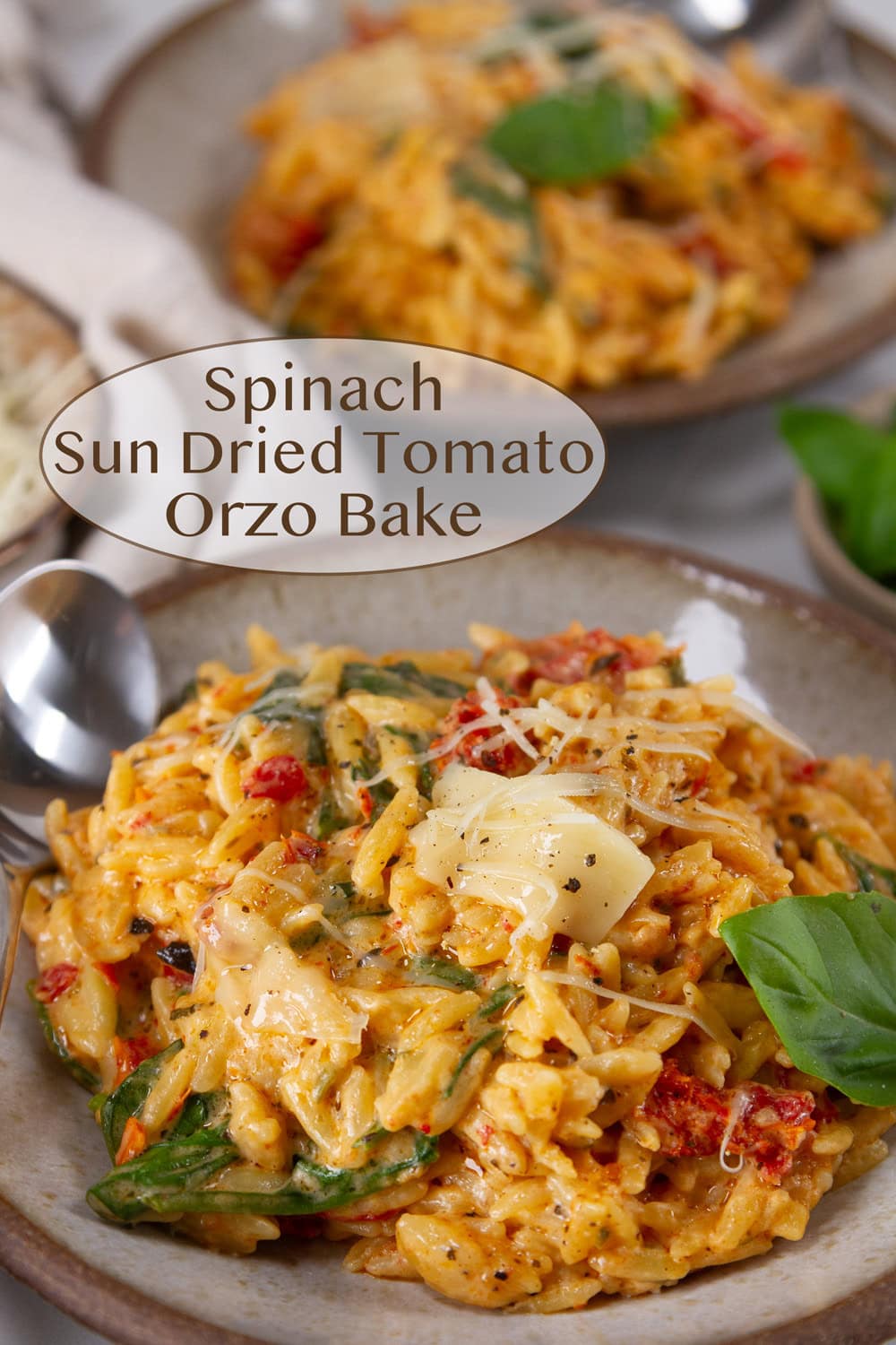 two servings of Spinach Sun Dried Tomato Orzo Bake with fresh basil on white plates.
