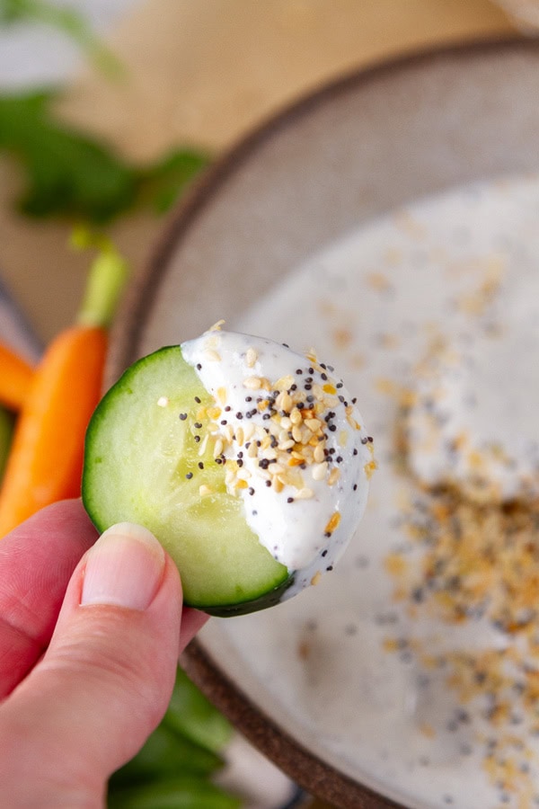 a cucumber slice dipped in creamy dip being held by a hand.