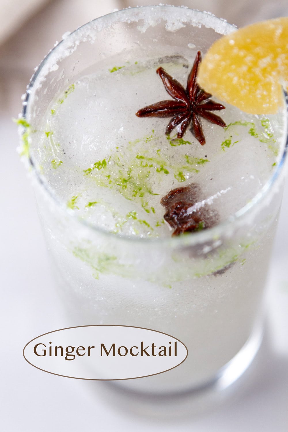 Looking down into a glass of Ginger Mocktail drink garnished with lime zest, ginger slice, and star anise.