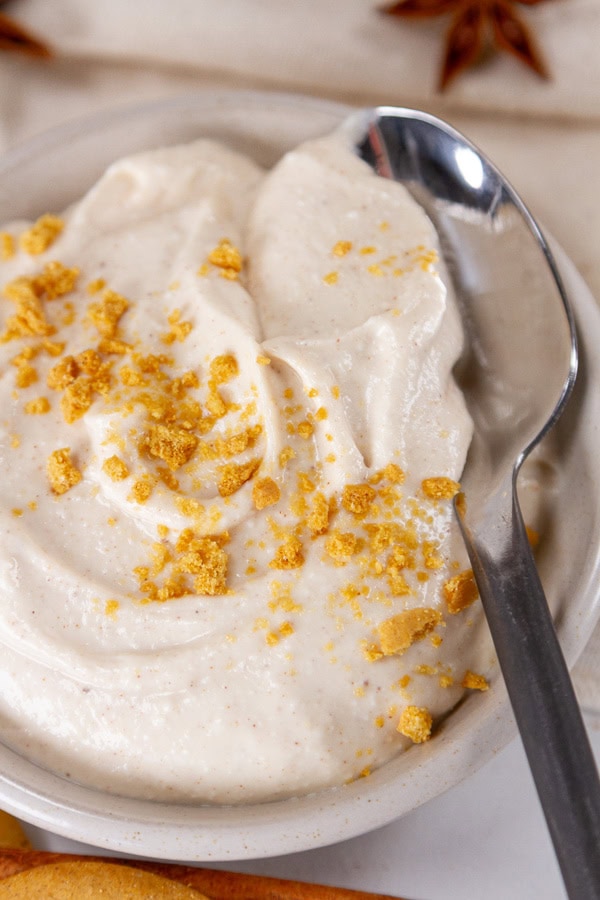 a close up on a cup of pudding with a spoon in it and its topped with crumbled ginger snap cookies.