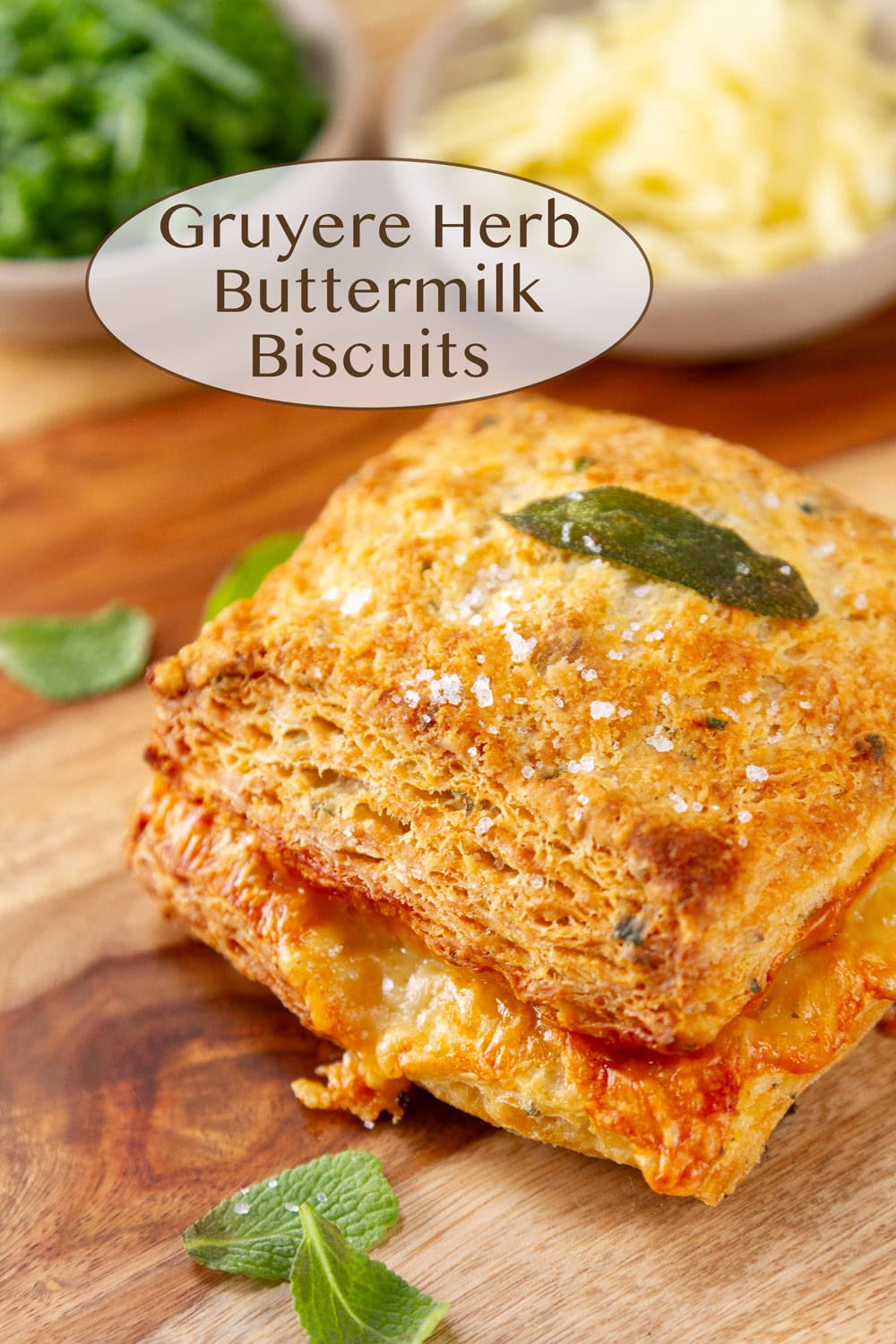a biscuit on a wooden cutting board with sage leaves some shredded Gruyere and chopped chives.
