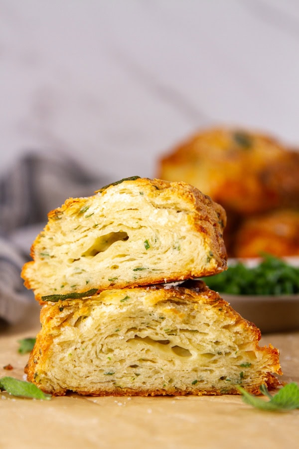 a flaky layered biscuit cut in half and stacked on top of itself with more biscuits in the background.