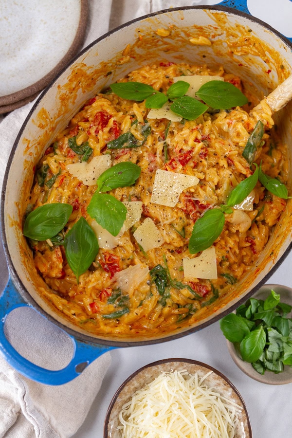 looking down into a casserole dish with baked casserole in it and a bowl of shredded Parmesan and a bowl of fresh basil nearby.