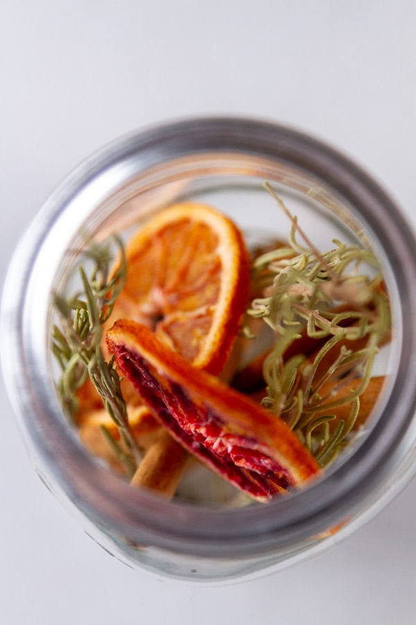 looking down into a mason jar with dried oranges, herbs and spices inside. 