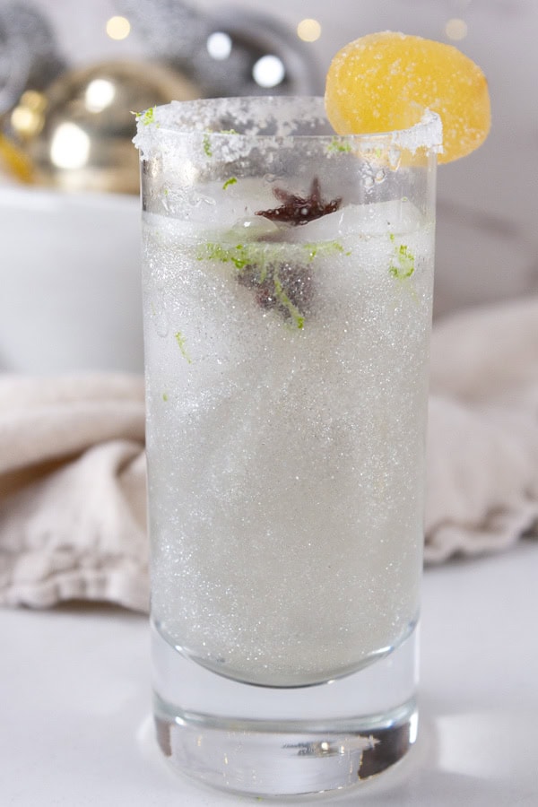 a ginger fizz mocktail with added edible glitter in front of a bowl of ornaments.