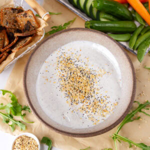 square crop looking into a bowl of creamy dip garnished with everything but the bagel seasoning and veggies and crackers around the bowl.