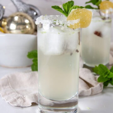 a highball glass with a drink and a sugared rim, mint and candied ginger garnish and ornaments in the background.