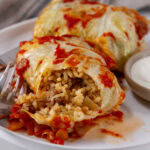 square crop of two cabbage rolls one is cut up so you can see the rice filling inside.