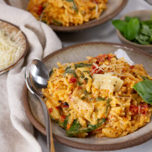 square crop of Spinach Sun Dried Tomato Orzo Bake on a serving plate with a spoon.