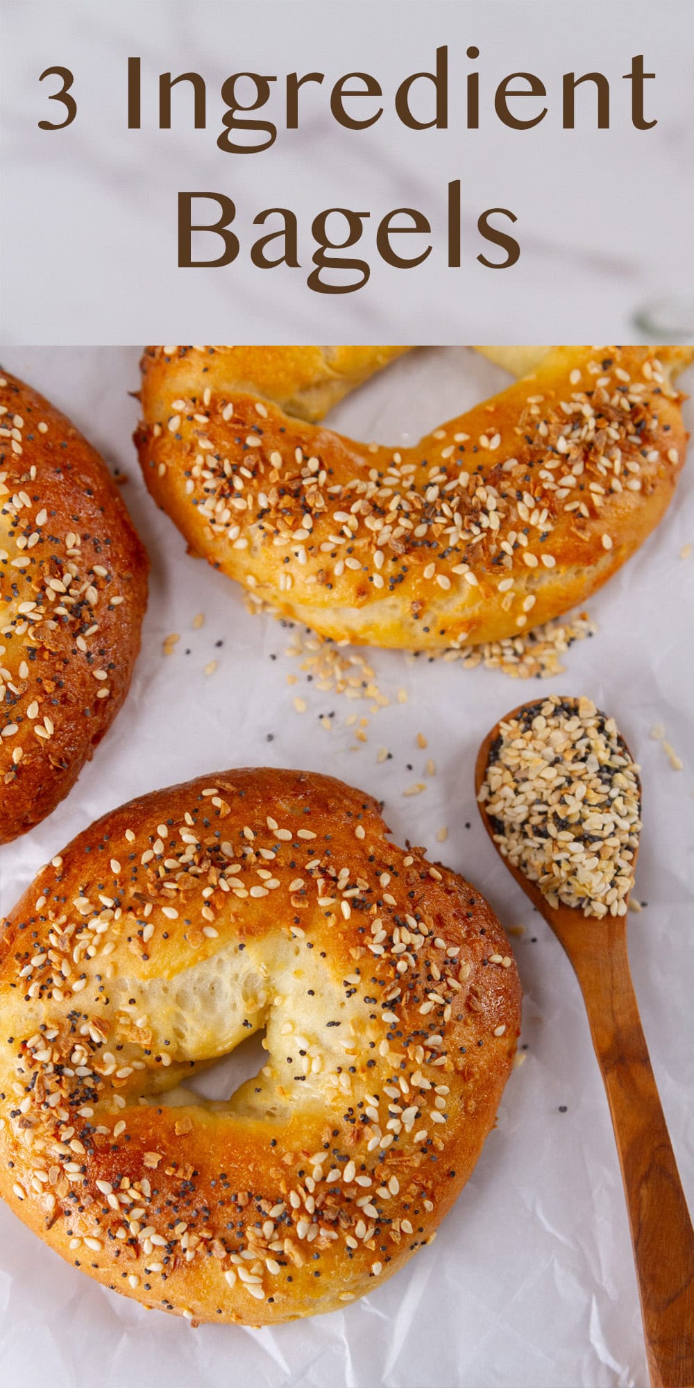 some everything bagel seasoning bagels on parchment paper with a wooden spoon full of seasoning next to them.