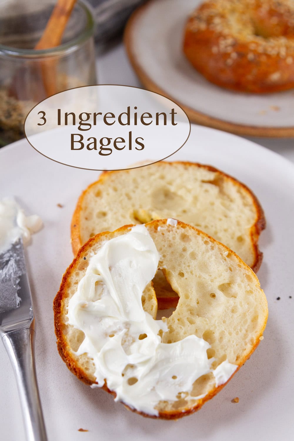 a bagel, cut in half with some cream cheese spread on part of it with a knife next to it.