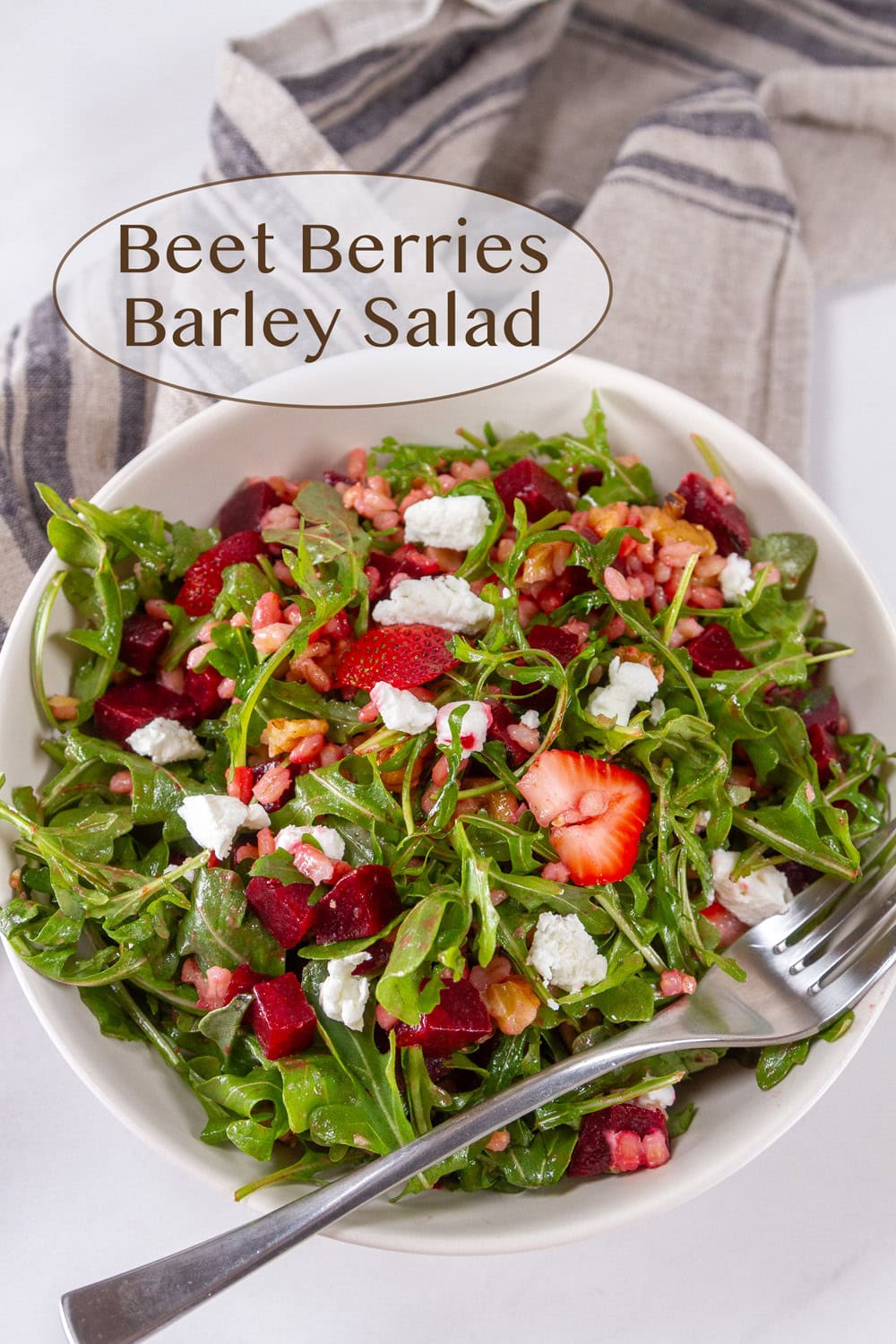 a salad with arugula strawberries, goat cheese with a fork in the bowl.