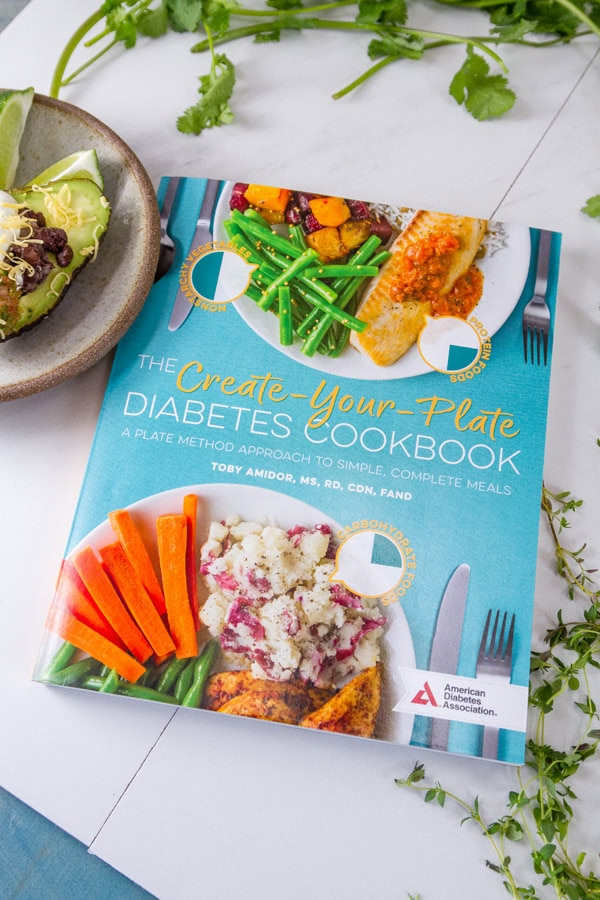 The Create-Your Plate Diabetes Cookbook: A Plate Method Approach to Simple, Complete Meals by Toby Amidor, MS, RD, CDN, FAND on a white background with fresh herbs around.