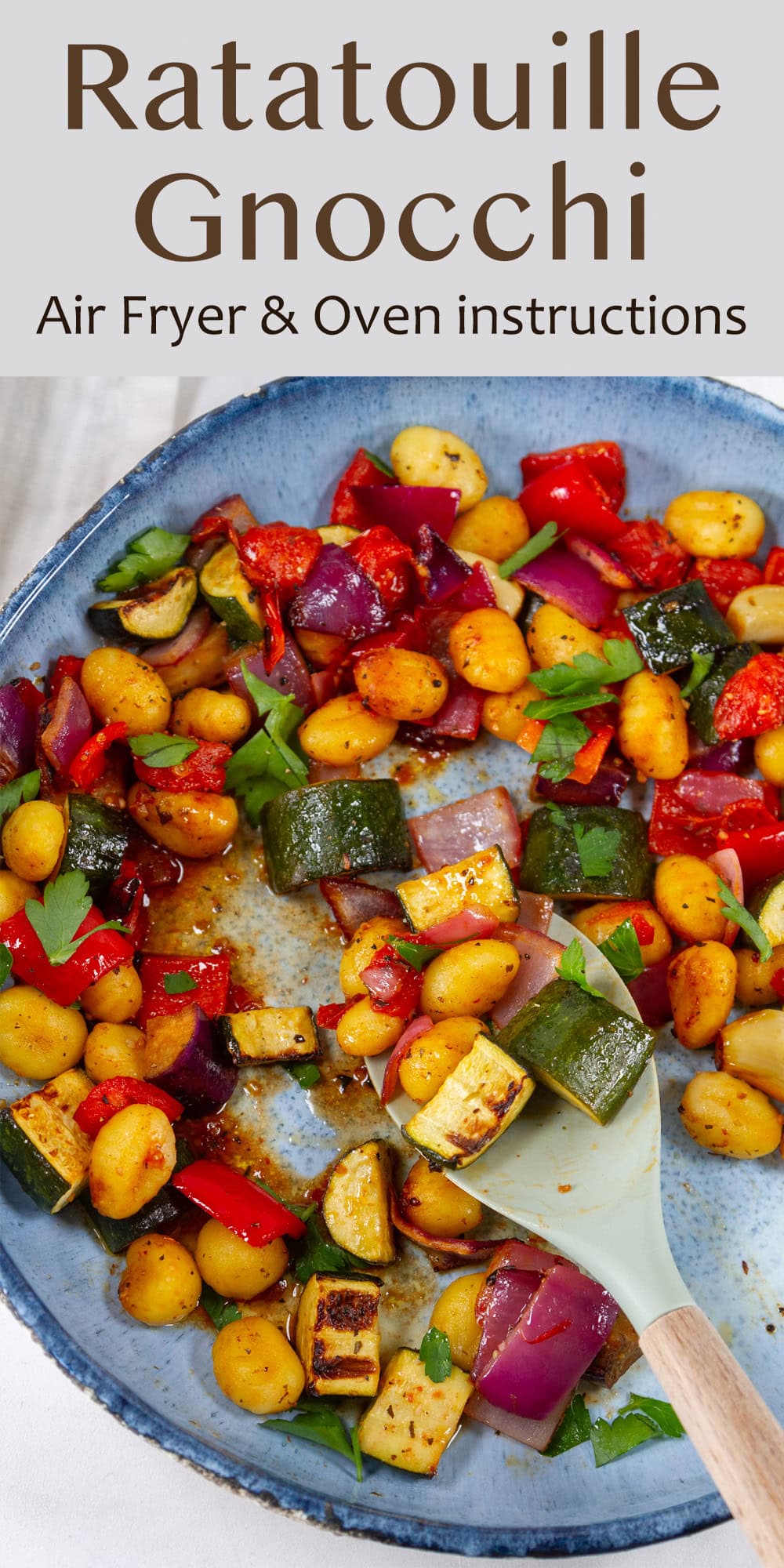 a blue bowl filled with roasted veggies and a spoon is resting in the bowl.
