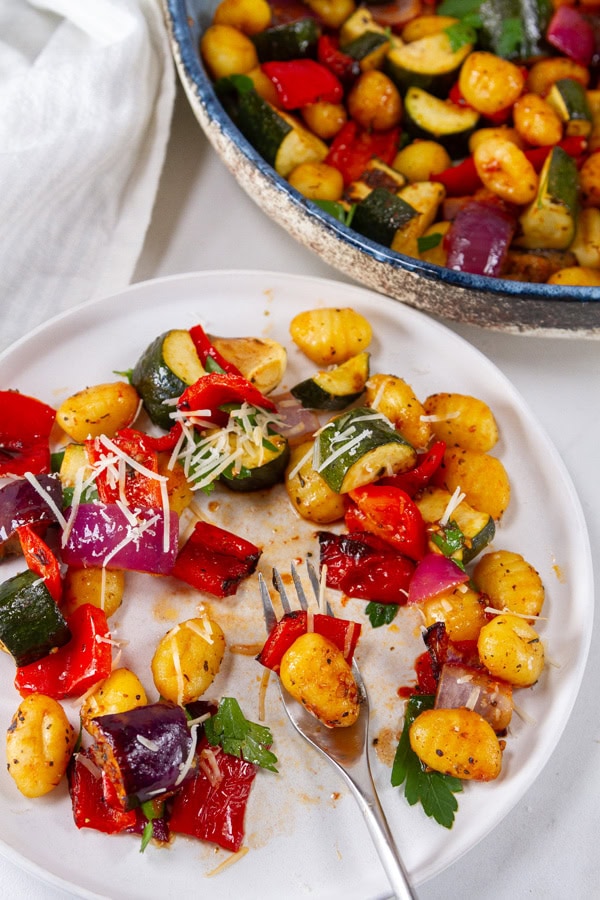 a dinner plate with Air Fryer Ratatouille Gnocchi and a fork next to a blue bowl of the dinner.
